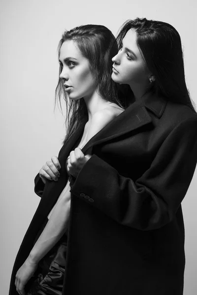 Mody strzał dwie eleganckie piękne dziewczyny w studio na szarym tle, ubrany w płaszcz mężczyzn. Zakupy inspiracji. Fotografia monochromatycznych (czarno-biały) — Zdjęcie stockowe