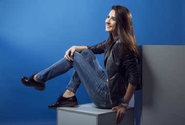 Kadın güzellik kavramı. Kot pantolon ve siyah ceket mavi arka plan üzerinde poz şık genç kız portresi. Mükemmel saç ve cilt. Vogue tarzı. Stüdyo vurdu