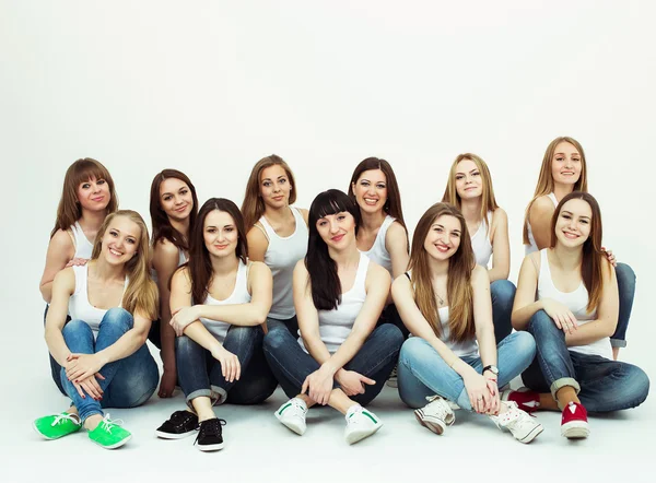 Joyeux concept ensemble. Portrait de groupe de filles en bonne santé en t-shirts blancs et en jeans bleus assis et posant sur fond blanc. Espace de copie. Style urbain. Plan studio — Photo