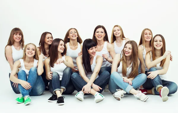 Joyeux concept ensemble. Portrait de groupe de filles en bonne santé en t-shirts blancs et en jeans bleus assis et posant sur fond blanc. Espace de copie. Style urbain. Plan studio — Photo