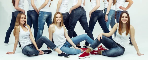 Joyeux concept ensemble. Portrait de groupe de filles en bonne santé en t-shirts blancs et en jeans bleus assis et posant sur fond blanc. Espace de copie. Style urbain. Plan studio — Photo