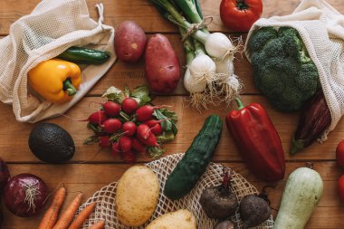 Doğal ahşap bir zeminde bez torbalarla taze sebzelerle dolu bir hayat.