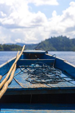 Küçük bir adanın önünde, denizin ortasında ilkel mavi bir tekne, seyahat konsepti. dikey