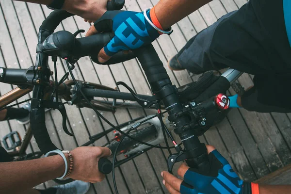 View from above the hands of cyclists riding their bikes. Hands of two cyclists holding the handlebars of their bikes with a wooden floor outside. sport concept. cycling concept. Horizontal