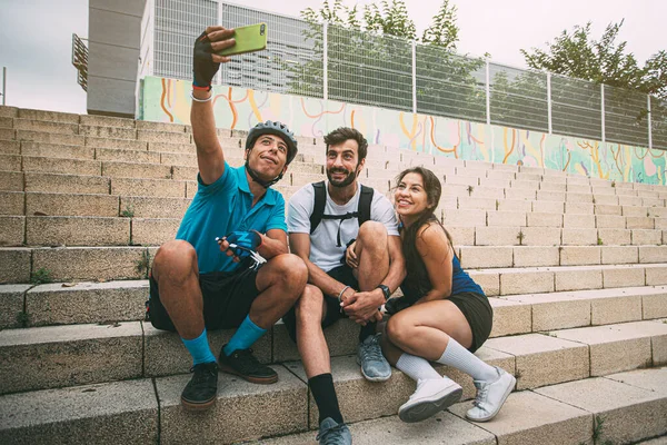 A group of happy, smiling friends dressed in sportswear sitting on urban stairs making a selfie with a mobile phone. Friends taking a picture with their smartphone in an urban setting. background with copyspace. Free time concept. Friendship concept.