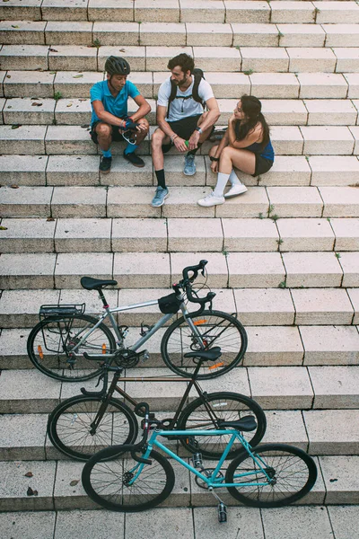 group of friends dressed in sportswear sitting on city stairs next to their bikes seen from above. Group of friends resting next to their bikes. background with copyspace. Urban sport concept. Free time concept. Friendship concept