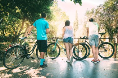 Bir grup genç arkadaş bisikletleriyle açık hava parkında doğa tarafından nehre bakıyorlar. Kopyalama alanı olan bir arkaplan. dostluk kavramı