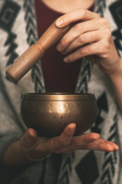 El yapımı panço giymiş, meditasyonda altın bir Tibet kâsesi kullanan bir kadının elleri. Kopyalama alanı olan arkaplan konsept meditasyon. dikey resim