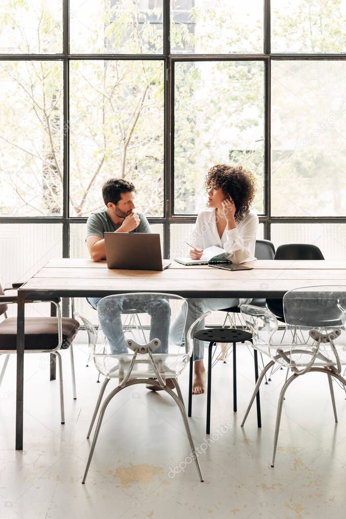 Young multiracial people interacting in bright co working loft office with big window. Coworkers concept. Vertical image. Business meeting concept. Startup concept. Copy space.