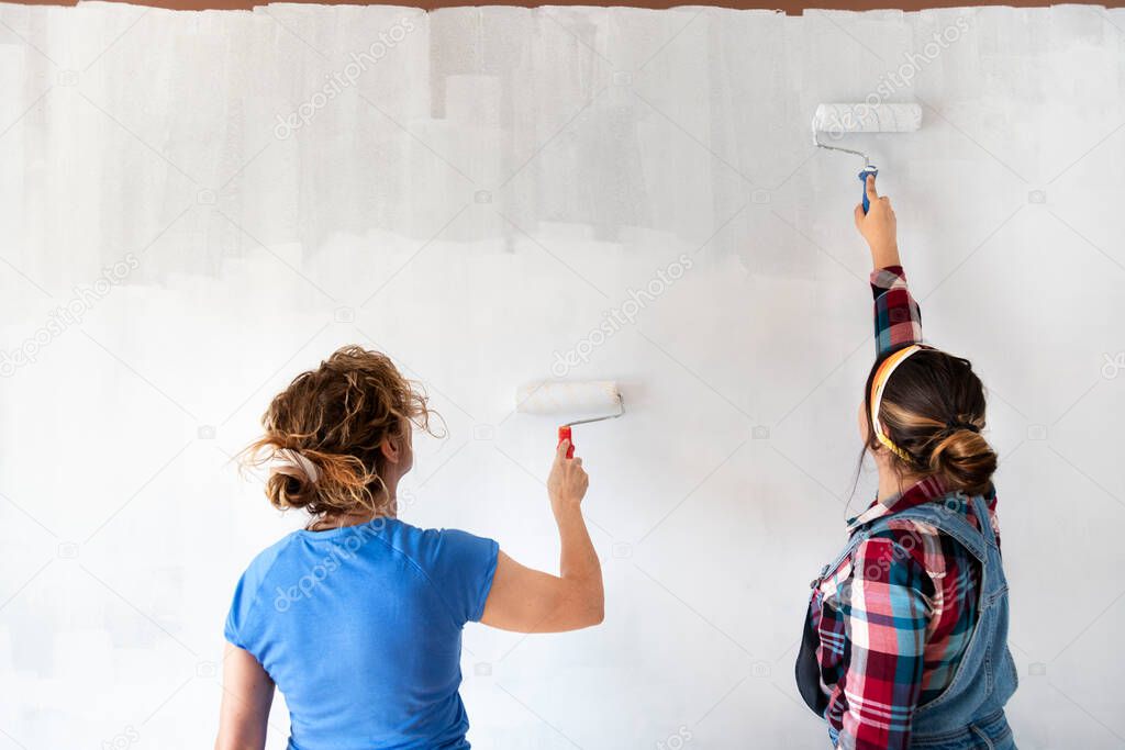 Two women painting new apartment walls in color white with paint roller. Renovating home. Real estate concept. Copy space