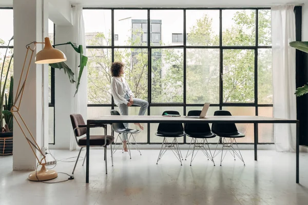 Young mixed race woman relaxing looking out the window in a bright spacious living room loft. At home concept. Copy space
