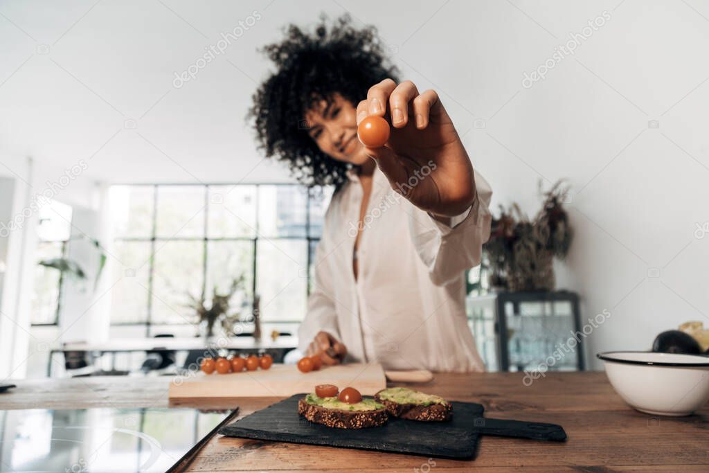 Young woman showing a tomato looking at camera. Selective focus on hand and tomato. Home concept. Cooking concept. Copy space