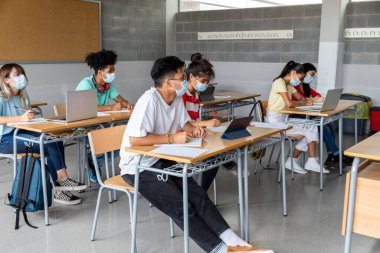 Sınıftaki bir grup çok ırklı lise öğrencisi koruyucu maskeler takıyor. Eğitim konsepti. Sağlık hizmetleri kavramı.