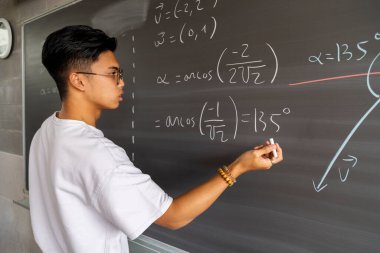 Asyalı ergen liseli çocuk tebeşirle tahtada matematik çözüyor. Eğitim kavramı.