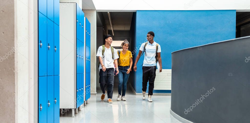 Group of teen high school students laughing walking in school corridor. Horizontal banner image. Copy space. Back to school. Education concept.