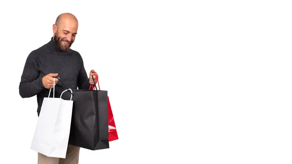 Joven hombre caucásico mira dentro de la bolsa de compras con satisfacción sobre fondo blanco. Banner horizontal. Copiar espacio. —  Fotos de Stock