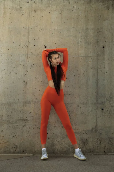 Sportovkyně v oranžovém sportovním oblečení, odpočívající na protahování tricepsů. Žena stojící tréninkové oblečení. — Stock fotografie