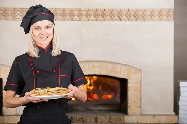 女厨师站在厨房入口与背景的披萨餐厅厨房木烤箱 — 图库照片