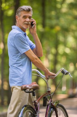 Onun bisiklet ile üst düzey adam parkta telefonla konuşuyor.