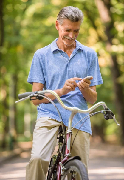 Senior Mannen Tittar Telefonen Medan Ridning Cykel Park — Stockfoto