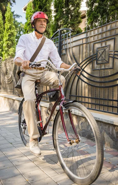 Senior man in helmet is riding bike in the street in town. Concept of active life elderly people.