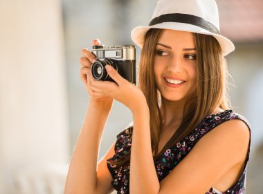 Şapkalı genç güzel kadın eski moda fotoğraf makinesi ile açık havada resim alıyor.