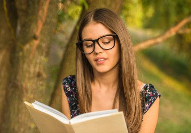 Genç güzel kadın parkta otururken bir kitap okuyor.