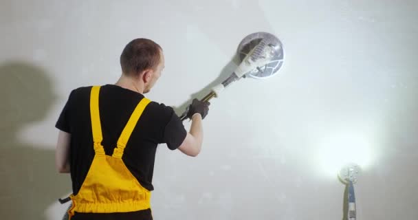 Шлифовальные стены для живописи. Работник в жёлтом рабочем костюме шлифует стену перед покраской специальным шлифовальным инструментом. DIY дом ремонтирует. — стоковое видео