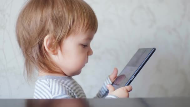 Vista lateral pequeño niño lindo sosteniendo una tableta digital viendo dibujos animados. Niños Gadget Adicción. — Vídeo de stock