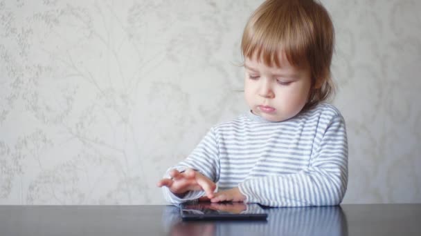 Divertido niño caucásico usando tableta sentada en la mesa — Vídeo de stock