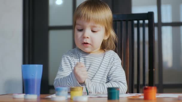 Grabben målar med färg och pensel sittande vid bordet. Utbildningsverksamhet för barn. — Stockvideo
