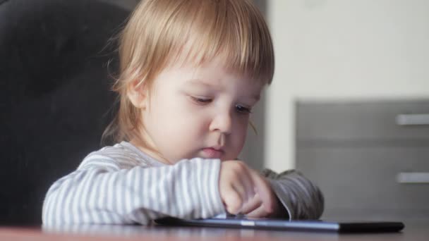 Lindo niño usando un dispositivo digital mientras está sentado en un escritorio. Niños gadget adicción. — Vídeo de stock