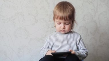 Küçük bir çocuk dijital tablet tutuyor ve elektronik bir cihazın ekranına dokunuyor. Erken çocukluk gelişimi için modern dijital aygıtlar