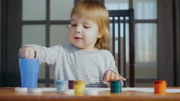 Детское творчество. Развитие ребенка. Ребенок сидит за столом и рисует красками и листом бумаги. — стоковое видео
