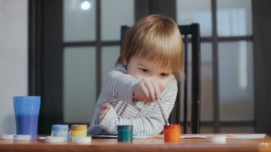 The kid is engaged in drawing with a brush using gouache paints.