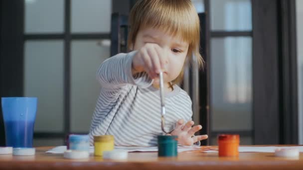 Toddler dipping a brush into a pot of paint. Kid engaged in drawing with gouache — Vídeos de Stock