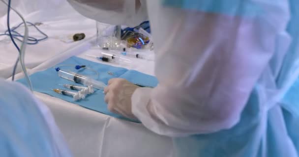 Κοντινό πλάνο του χεριού ενός γιατρού ή νοσοκόμου που αγγίζει ένα χειρουργικό όργανο και βοηθά το γιατρό χειρουργό κατά τη διάρκεια μιας επέμβασης στο χειρουργείο — Αρχείο Βίντεο