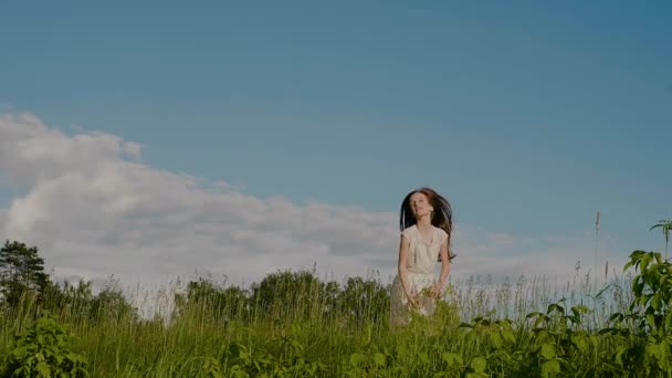 Feliz niña en edad escolar en un vestido blanco vomita la corona de flores silvestres y saltar sobre el fondo de la naturaleza. — Vídeos de Stock