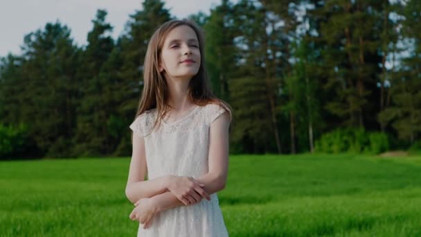 Happy Caucasian school age girl in white dress on background of trees and green grass. Oneness with Nature. — Stock Video