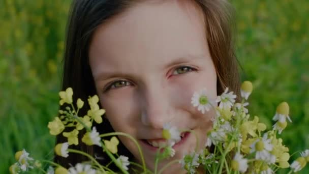 Porträtt av glad leende skolålder flicka med vilda blommor tittar på kameran. — Stockvideo