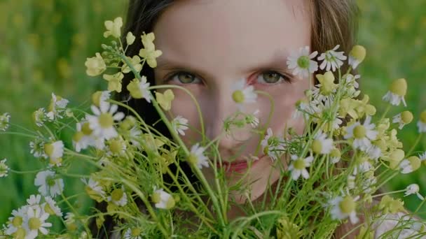 野の花の花束を通して見て女の子の顔のクローズアップ. — ストック動画