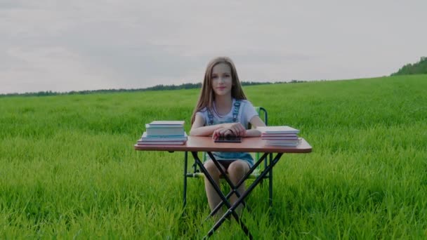 Навчання на відкритому повітрі. Дівчина шкільного віку сидить за столом з книгами, оточеними природою — стокове відео
