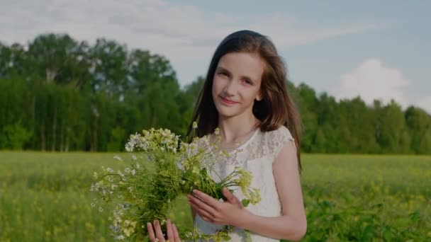 Joyeuse fille souriante tient une couronne de fleurs sauvages dans les mains et regarde la caméra. — Video
