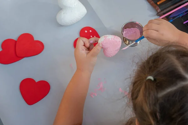 child hands paint the heart with pink paint and a brush
