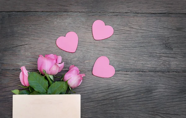 粉色的三颗心 粉色的玫瑰 装在纸袋里 木制底座上有复制的空间 — 图库照片