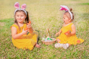 Çocuklar Paskalya tavşanının kulağındaki açıklığa oturur. Kızlar havuç kemirir ve bir sepet Paskalya yumurtasıyla oynarlar.