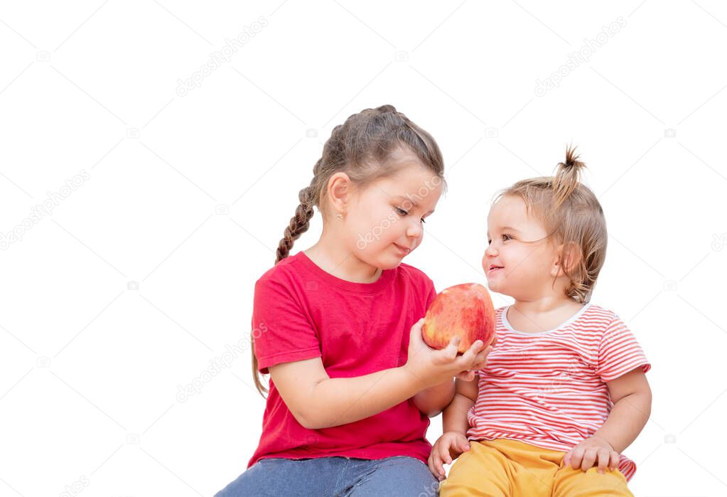 Two children share an apple. A girl holds out an apple to her younger sister.