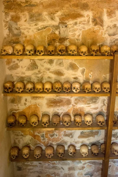 Three wooden shelves lined with human skulls. Spinalonga leper colony in Crete