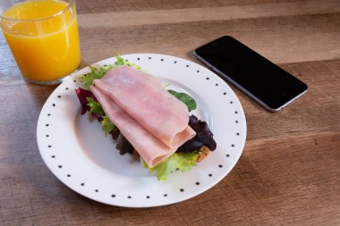 Güne başlamak için sağlıklı bir kahvaltı, taze portakal suyu ve jambonlu tost. Masada cep telefonu, yaşam tarzı..