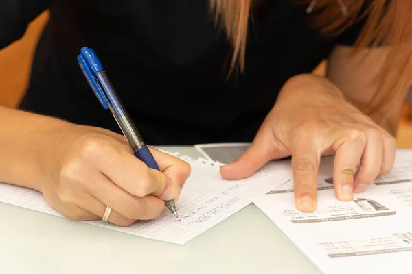 Kadın kuaför resepsiyona bir müşteri için ürün tahmini yazıyor. Müşteri tarafından seçilen listeden ürünlerin fiyatlarını ve ürünlerini yazıyor. O bir kalem ve kağıt taşıyor..